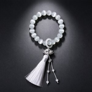 White cat's eye feng shui mala bracelet with silver lotus charm and white tassel on dark gray background